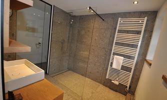 A modern bathroom with a glass shower and a sink. The walls are made of gray stone, and a towel holder is visible.