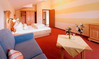 A cozy hotel room with a blue sofa and a wooden table. The wall is painted light with yellow stripes, and there is a view of the bed and a wardrobe.