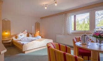 A cozy room with a double bed and colorful chairs. Light falls through a large window, creating a bright atmosphere.