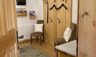 A cozy entrance area with wooden decor. There are two chairs, a coat rack, and a rug on the floor.