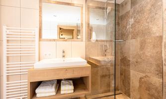 A modern bathroom with a stylish shower and a wooden vanity. The walls are clad with elegant tiles in earthy tones.