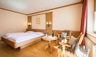 A cozy room with a double bed and a small table. There is an armchair and a bright, inviting atmosphere.