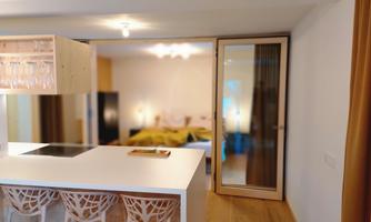 A modern kitchen with a clean design and a bar. In the background, a bedroom with warm colors is visible.