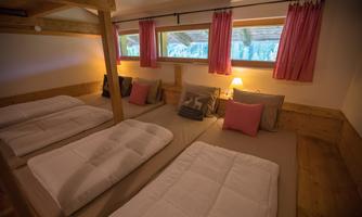 A cozy room with multiple beds and wooden ceilings. The windows are decorated with pink curtains and offer a view of the outdoors.