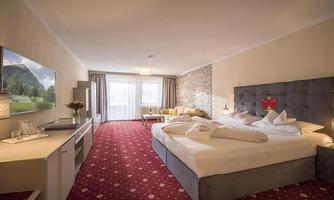 A modern hotel room with a large bed and a cozy seating area. The room has a television and large windows that let in plenty of daylight.
