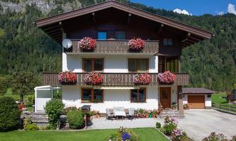 A charming old house with blooming flower boxes at the windows. Surrounded by a green meadow and mountains in the background.