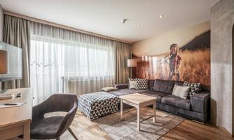A modern living room with a large sofa and a wooden table. One wall features a creative mural of a person in nature.