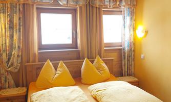 A cozy bedroom with two beds and yellow blankets. The walls and curtains are in warm colors, and there are windows with views outside.