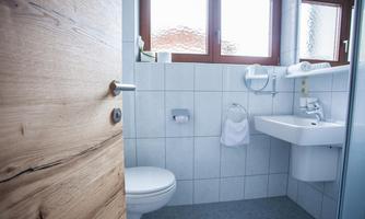 A modern bathroom with bright tiles and large windows. It includes a toilet, a sink, and some towels.