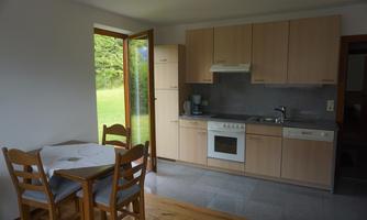A modern kitchen with wood and gray furniture. A table with chairs is in a bright room with a view of the greenery.