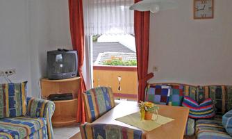 A cozy living space with colorful sofas and a table. A window with a view outside and a small TV unit are also present.