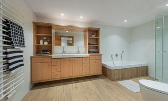 A modern bathroom with a wooden vanity and a large mirror. There is a bathtub and a spacious shower, as well as elegant towels on the wall.