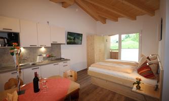 A cozy living kitchen with modern design and wooden elements. The bedroom is bright and inviting, with access to a balcony.