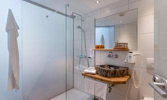 A modern bathroom with a glass shower and a stylish wooden vanity. The walls are brightly tiled and the lighting is cheerful.