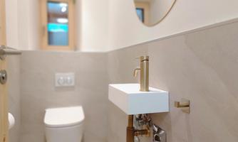 A modern bathroom with an elegant toilet and a small sink. A round mirror and a window provide light and a fresh impression.
