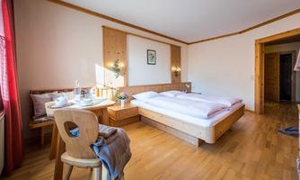 A cozy room with a double bed and wooden-paneled walls. A table stands next to the bed, decorated with flowers and a glass.