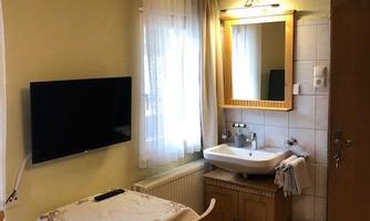 A cozy room with a table, two chairs, and a television. There is a sink and a large mirror on the wall.