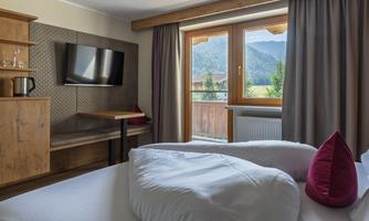 A modern room with a double bed and a television. Large windows offer a view of the mountains and let in plenty of daylight.