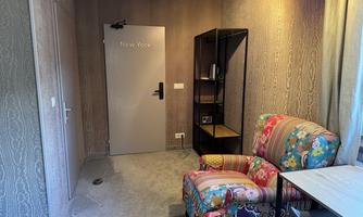 A cozy room with a colorful armchair, a table, and a bookshelf. The door to the inside is labeled "New York."