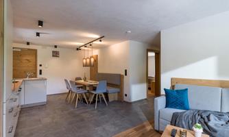 A modern living room with a cozy couch and a dining area. The room has light walls and an elegant, minimalist style.