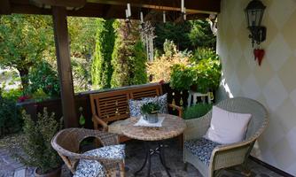 A cozy terrace with a round table and two chairs.  
Surrounded by green plants and a warm, inviting atmosphere.