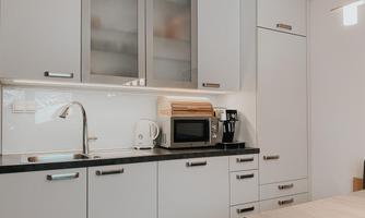 A modern kitchen with white cabinets and a black countertop. On the counter, there is a kettle, a microwave, and a coffee machine.
