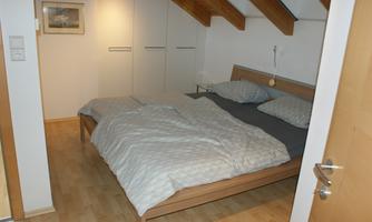 A cozy bedroom with a double bed and wooden surfaces. The room has sloping ceilings and bright colors.