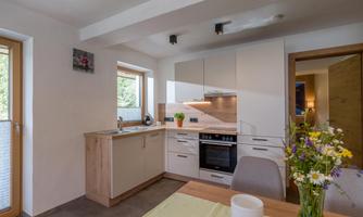 A modern kitchen with bright furnishings and large windows. Fresh flowers are in a vase on the table.