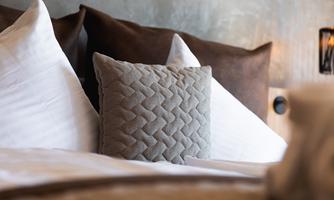 A cozy bed with decorative pillows in soft colors. In the background, a stylish lamp is visible.