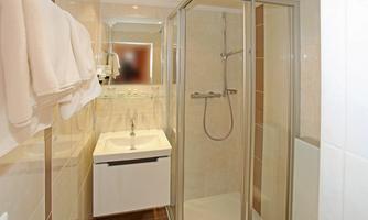 A modern bathroom with a shower and a sink. Towels hang on the wall and the tiles are bright and contemporary.
