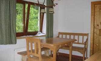 A cozy dining area with a wooden table and benches. Large windows let in plenty of light and offer a view of the green nature outside.