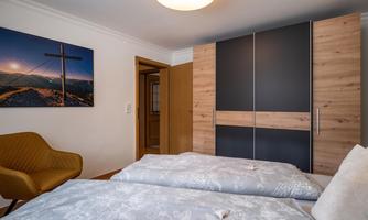 A cozy bedroom with two beds and a wooden wardrobe. On the wall, there is a picture of a landscape with a cross.