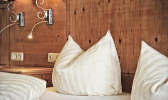 A cozy bedroom with white pillows on a bed. The walls are made of wood and there are modern wall lights.