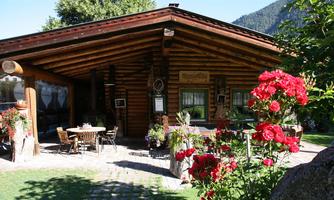 A pretty wooden house surrounded by colorful flowers. Outside, there are tables and chairs for guests.