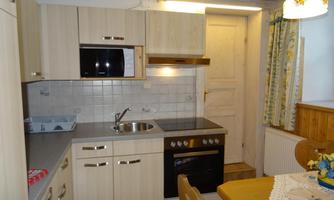 A modern kitchen with wooden surfaces and various appliances. The table is decorated with a crochet piece and there is a door leading to another room.