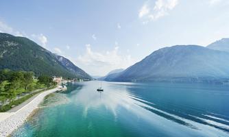 A calm lake surrounded by green mountains and clear blue sky. A small boat floats on the water.