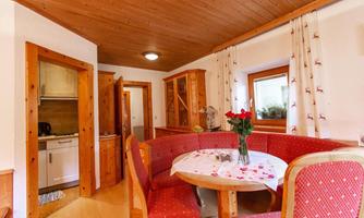 A cozy living kitchen with a round table and red chairs. The table is decorated with a flower vase and decorative flower petals.