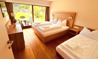 A cozy hotel room with two beds and a large window. The view overlooks a green landscape and a balcony.