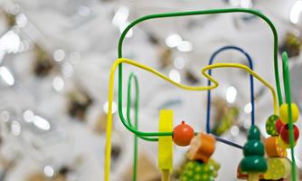 A colorful wooden toy with colorful beads and different shapes. Blurry, shiny objects can be seen in the background.
