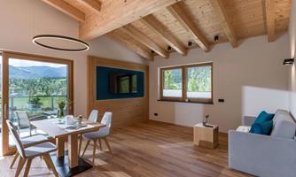 A modern living room with wooden ceilings and large windows. The space is bright and inviting, with a dining table and a cozy couch.