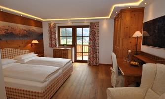 An inviting hotel room with two beds and wood paneling. Large windows provide a view of the landscape and allow for plenty of daylight.