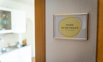 A sign reading "Village Apartment" hangs on a wall. In the background, a modern kitchen is visible.