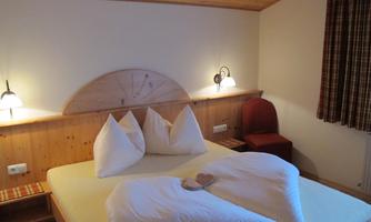 A cozy bedroom with a large bed and romantic pillows. The wooden ceiling and warm colors create an inviting atmosphere.