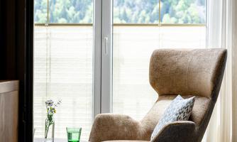 A cozy armchair sits next to a small table. Large windows with a view of green mountains let in plenty of light.