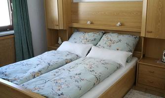 A cozy bedroom with a wooden bed and fresh bedding. There are wardrobes against the wall and the window is decorated with green curtains.