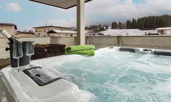 A hot tub on a terrace overlooking snow-covered hills. In the background, some houses and forests can be seen.