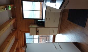 A modern kitchen with a wooden ceiling and large windows. The room has bright furniture and plenty of daylight.