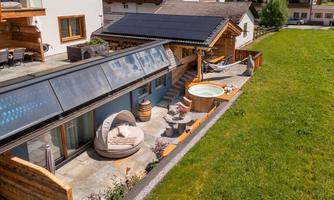 A modern house with a solar roof and a hot tub in the garden. The outdoor area is cozy with seating and a green lawn.