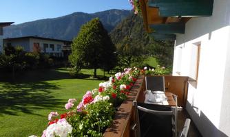 A beautiful balcony with colorful flowers and a view of green meadows and mountains. The sun is shining and the sky is blue.