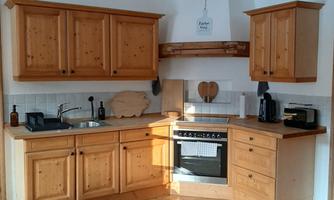 A modern kitchen with wooden cabinets and a stove in the center. The room has a cozy atmosphere with a rug on the floor.